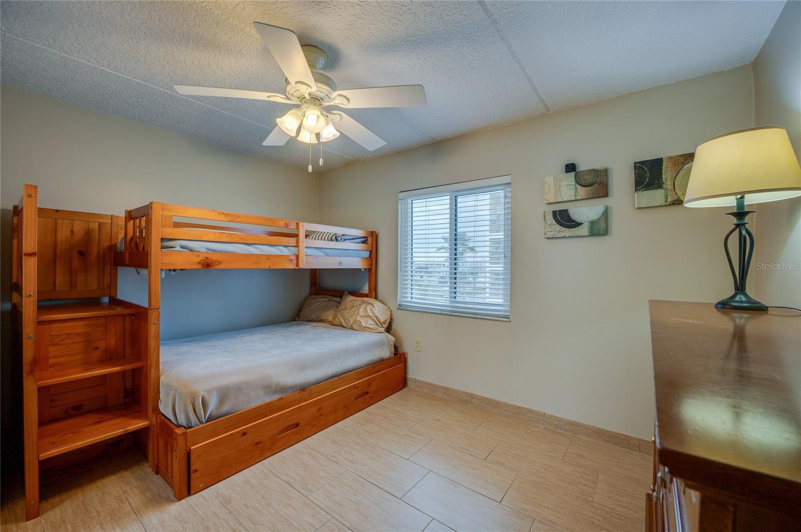 A bright and versatile second bedroom featuring tile flooring, a ceiling fan, and a large window for natural light—perfect for guests, a home office, 