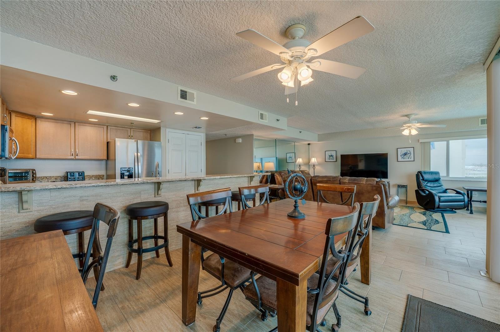 A central dining area connects to the kitchen and living space, all under ceiling fans and surrounded by windows—ideal for casual meals and gatherings