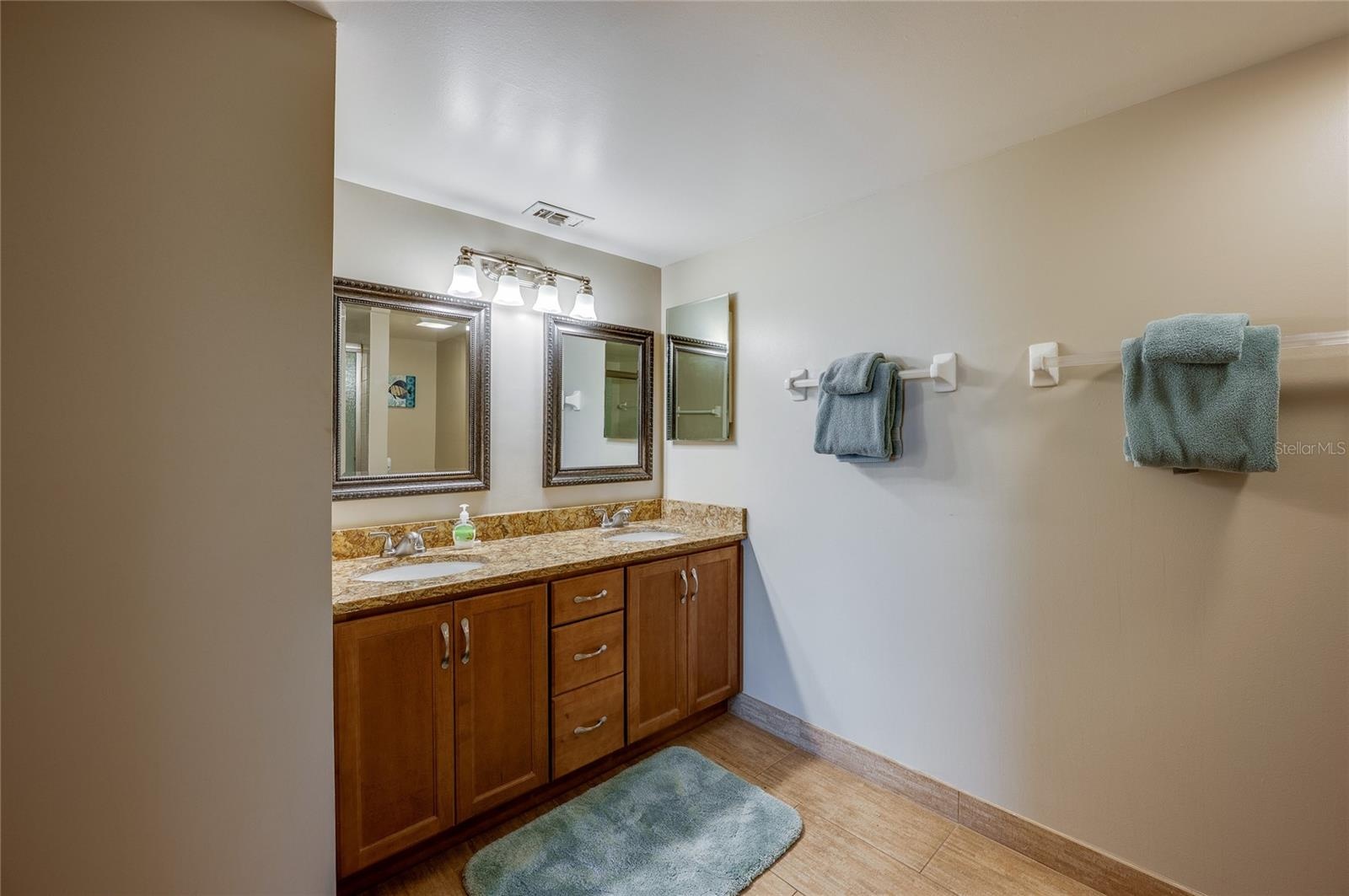 Dual mirrors with elegant framing and granite countertops top the double vanity, offering plenty of storage in warm wood cabinetry.