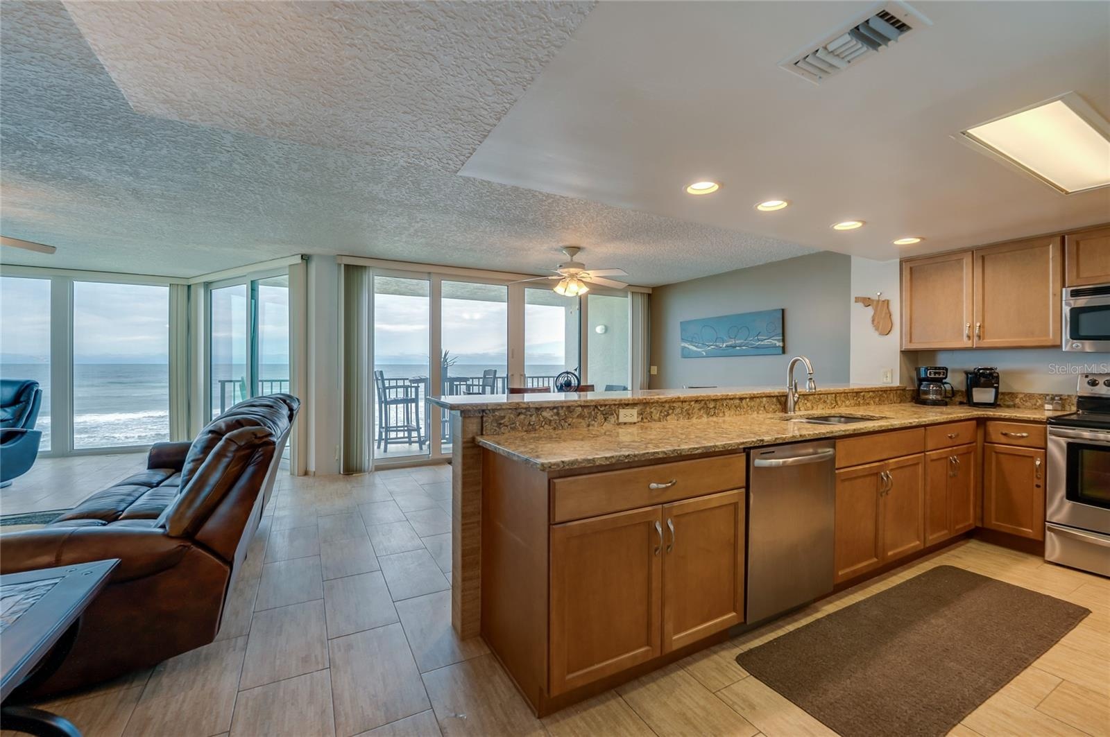 This open kitchen boasts granite countertops, stainless steel appliances, and a breakfast bar overlooking the ocean-facing dining space—perfect for en