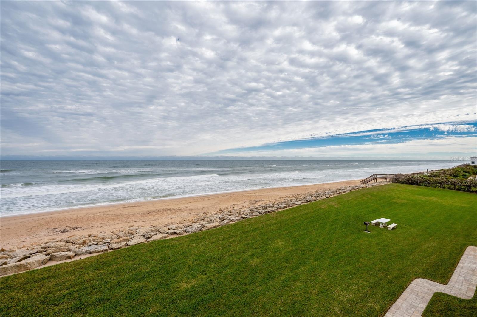 A lush green lawn frames wide ocean views and provides open space between the residence and the shoreline, ideal for outdoor lounging or play.