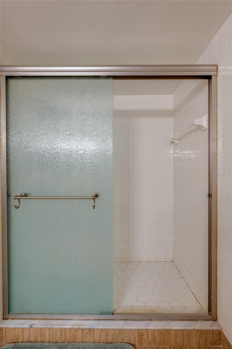 Close-up view of the primary suite’s shower showcases a hexagon tile floor and full tile surround behind frosted sliding doors.