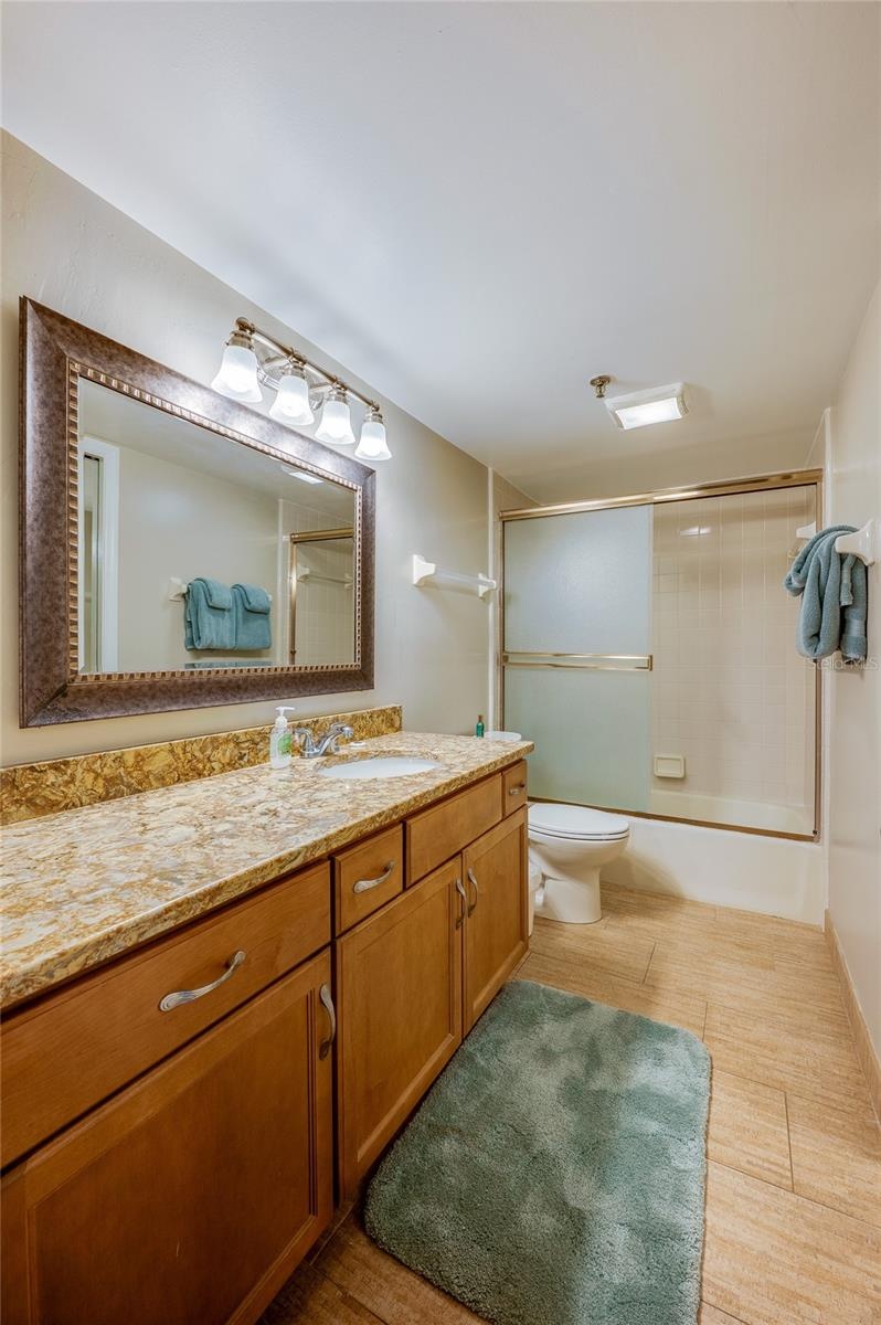 This full bath features a combination tub/shower with sliding doors, granite-look vanity, and framed mirror great for guests or shared use.