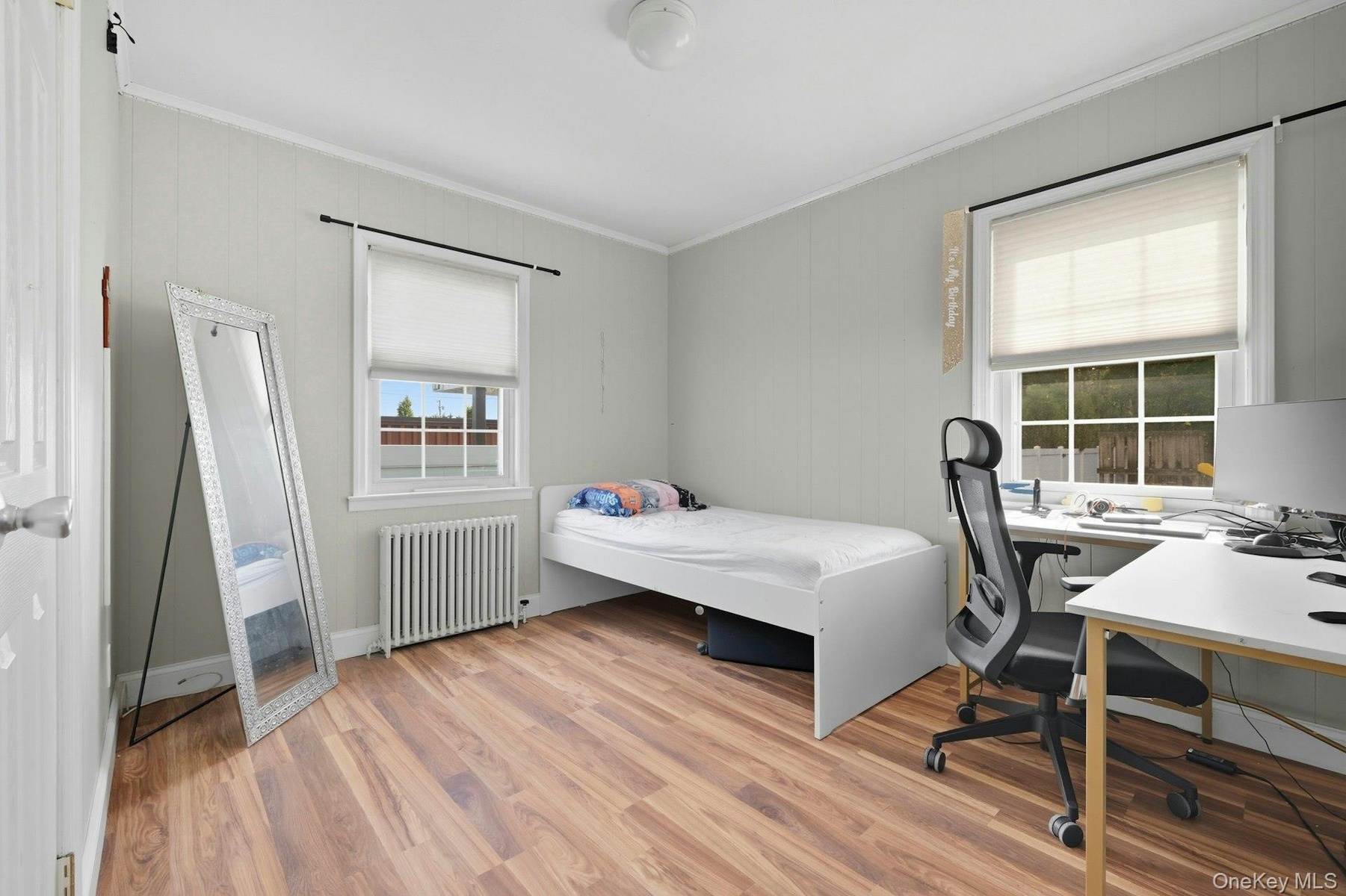 Bedroom with radiator heating unit, light wood-style floors, crown molding