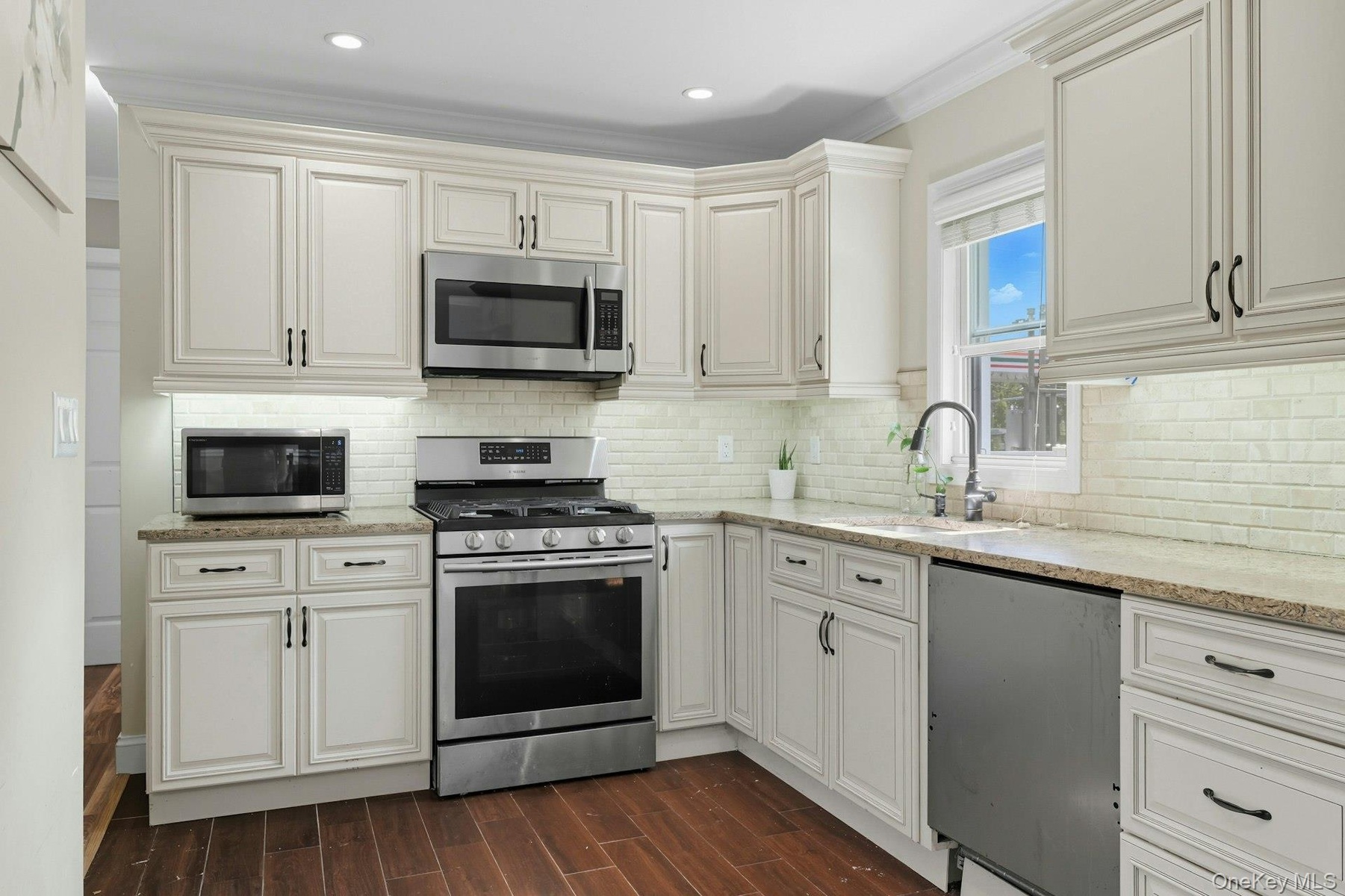 Kitchen with appliances with stainless steel finishes, wood tiled floors, light stone countertops, tasteful backsplash, and ornamental molding