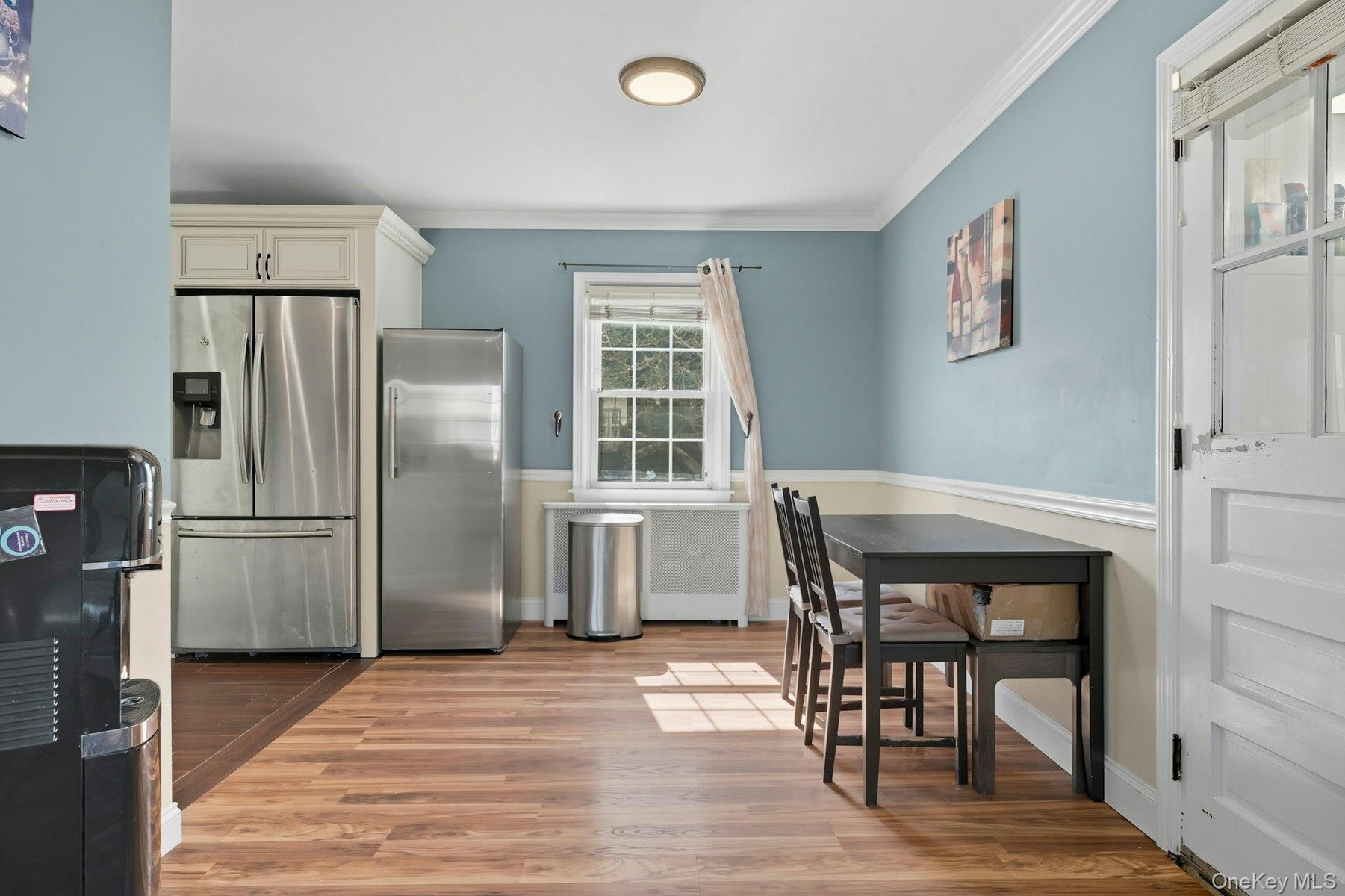 Kitchen with stainless steel fridge with ice dispenser, freestanding refrigerator, light wood-style flooring, ornamental molding, and radiator heating
