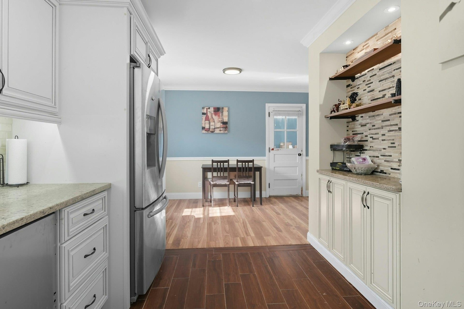 Kitchen with tasteful backsplash, white cabinetry, light stone countertops, and crown molding