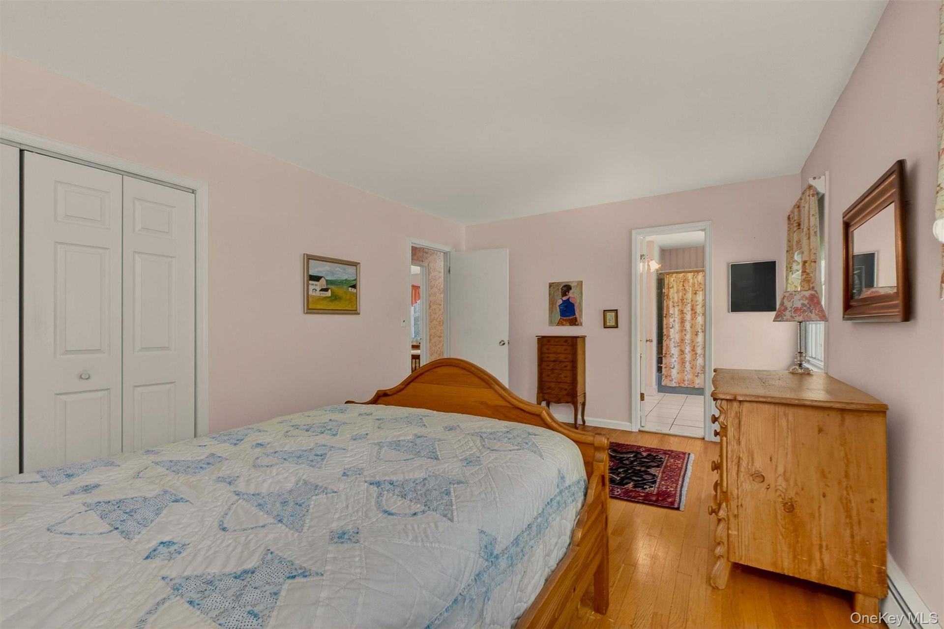Primary bedroom w/hardwood flooring & access to dual entry full bath, complemented by light-toned wall paint and white trim work
