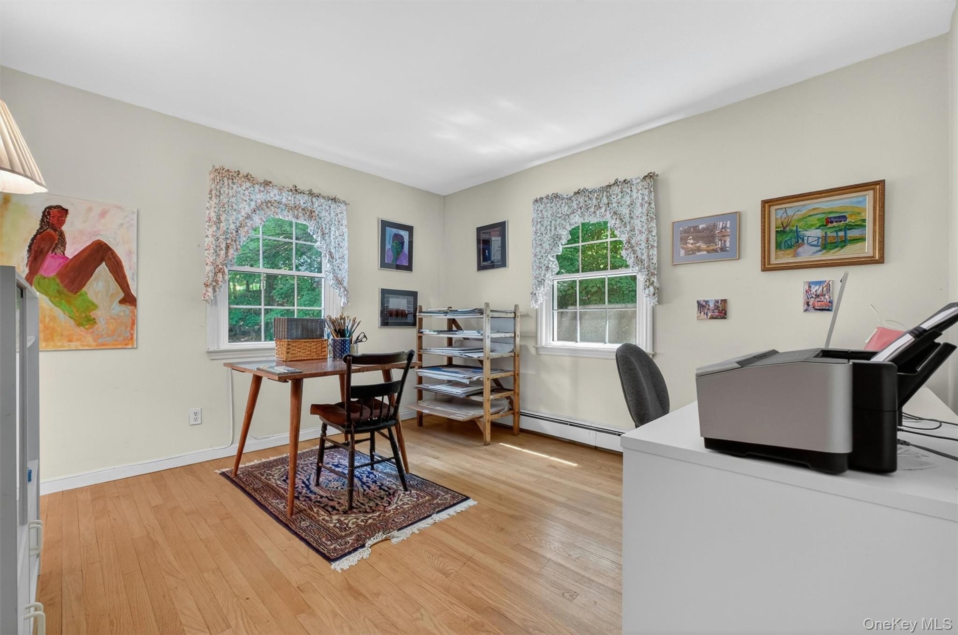 Bedroom #2 (used as office) w/light-toned walls, wood-finish flooring, two double-hung windows, and white trim baseboards