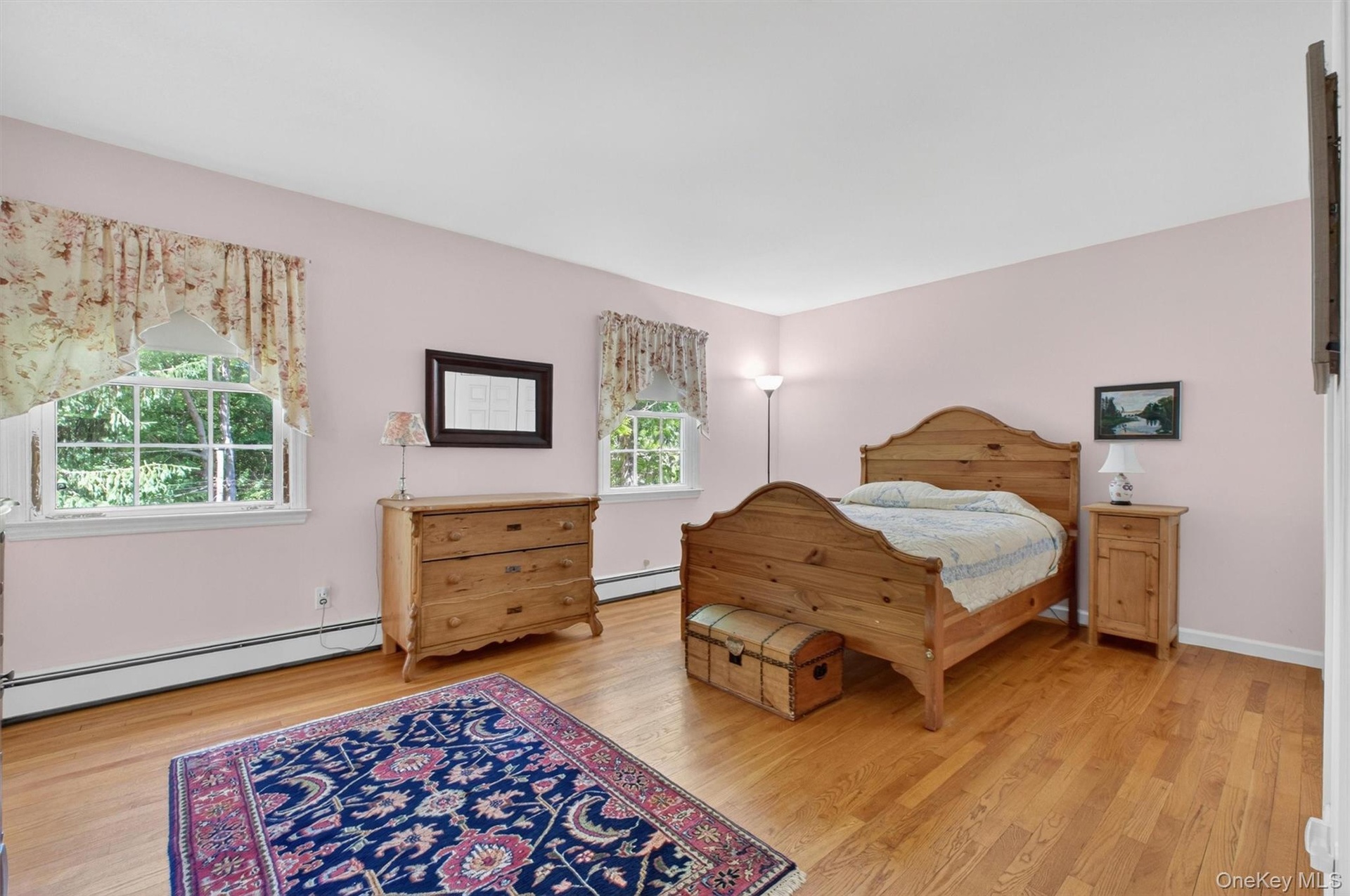Primary Bedroom w/Hardwood flooring throughout featuring two windows with white trim and a baseboard heating system