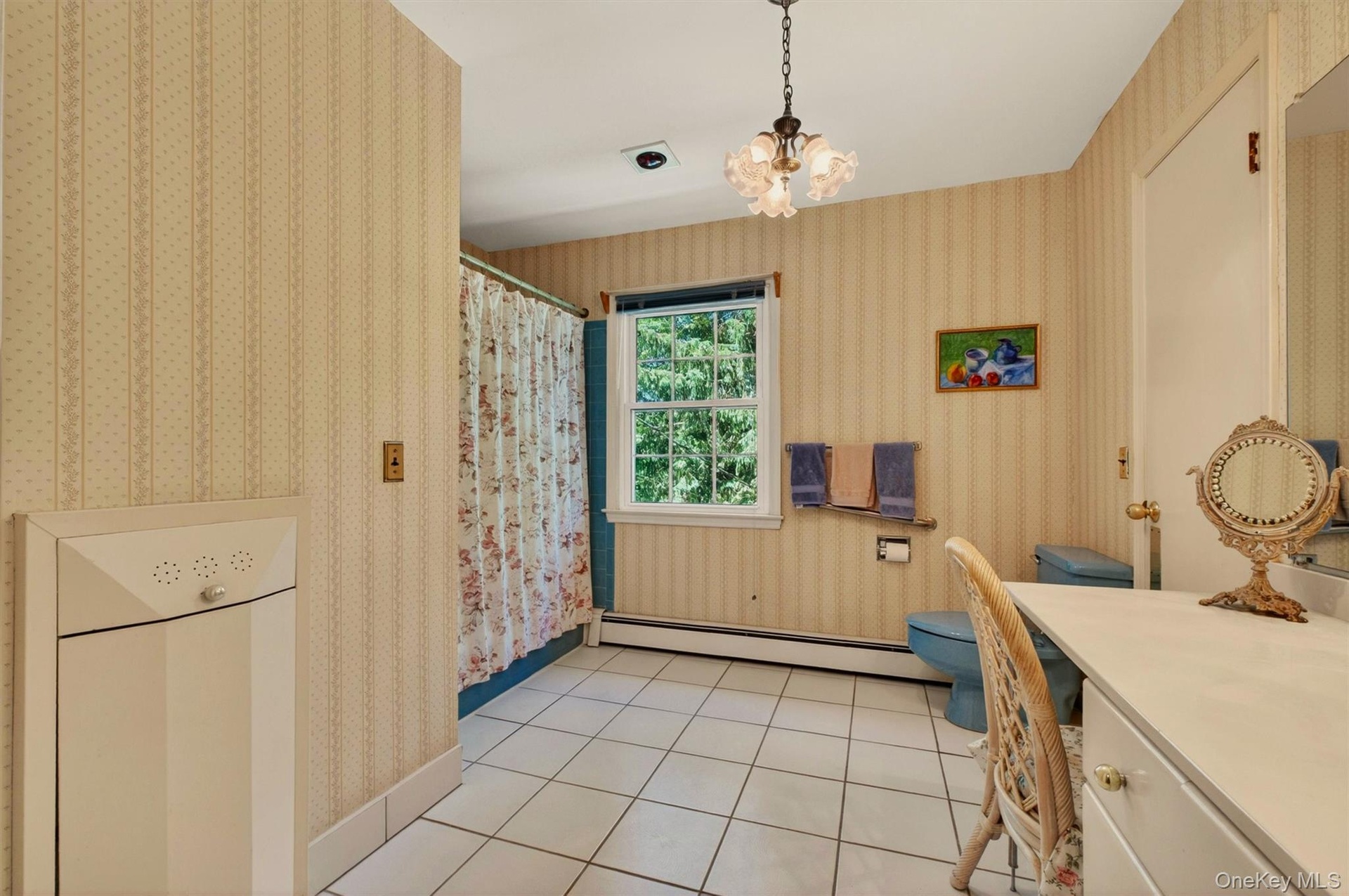 Bathroom featuring a vanity desk, white tile flooring, patterned wallpaper, a window, and a light fixture