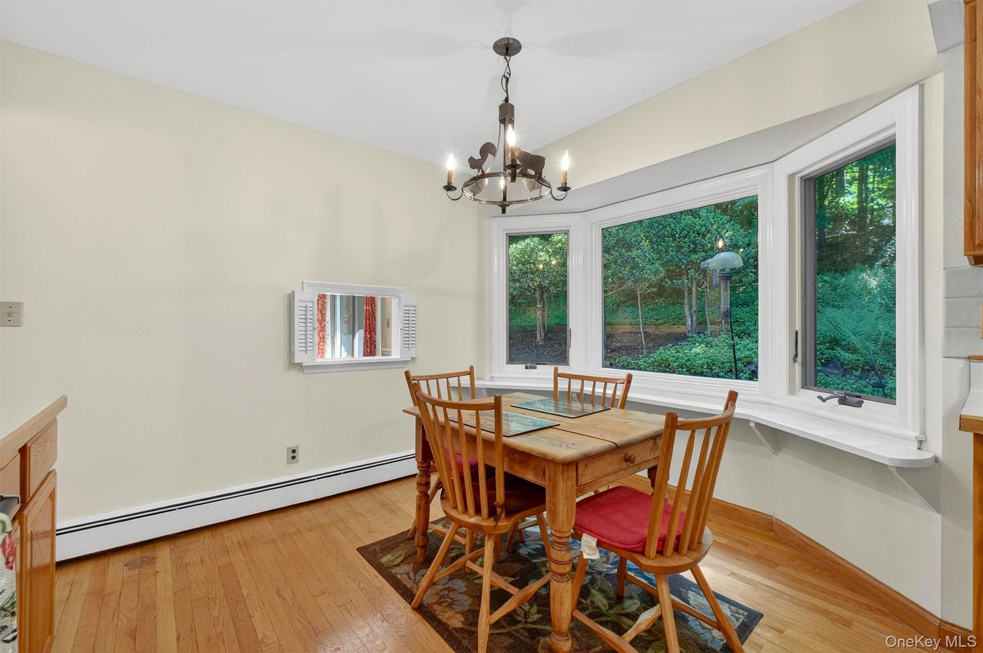 Bay window with exterior landscaping, wood-finish flooring, cream-toned walls, and a built-in kitchen counter with wood cabinetry