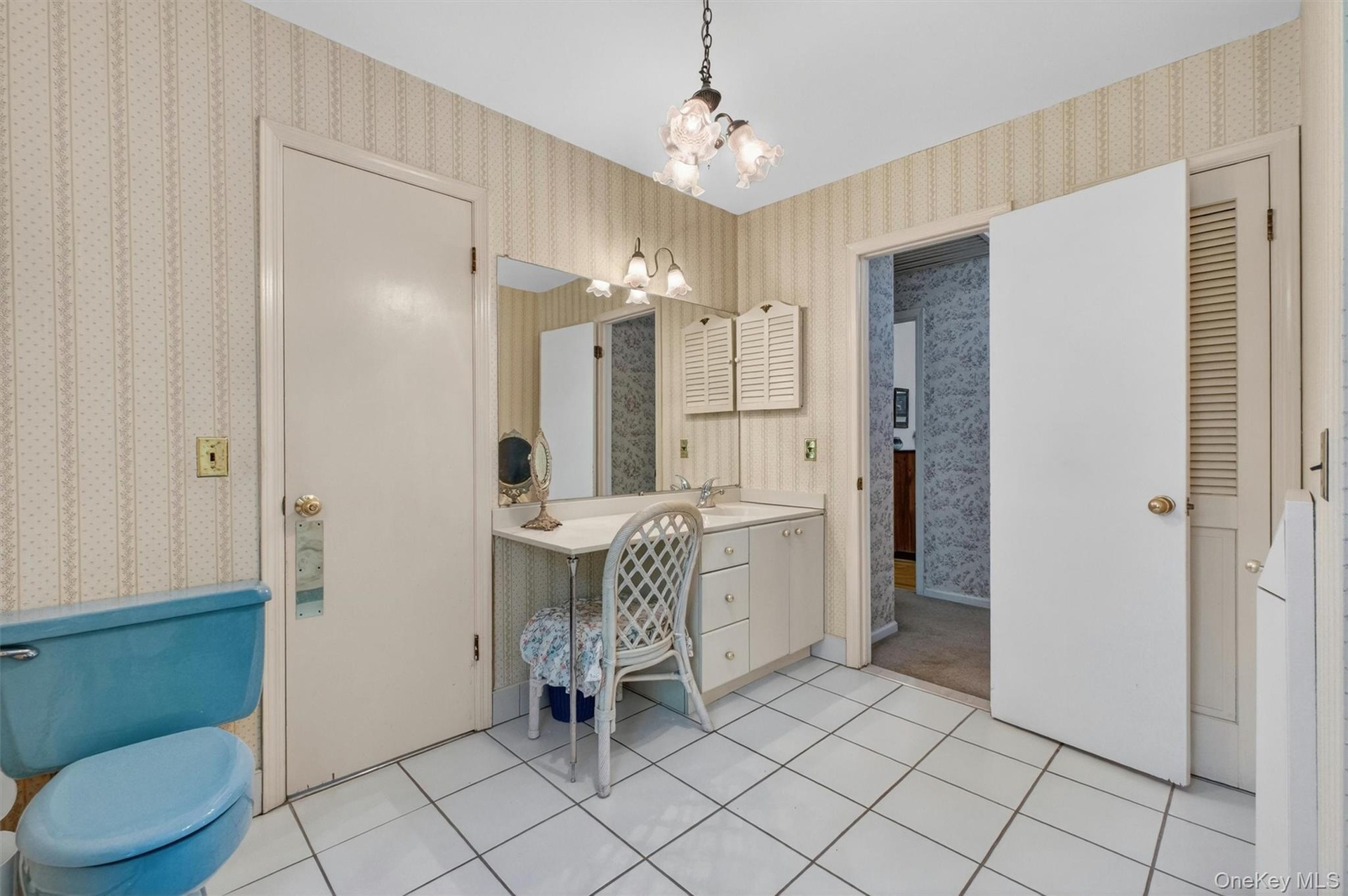 Bathroom with white ceramic tile flooring, a single vanity with storage, a makeup vanity, and two paneled doors