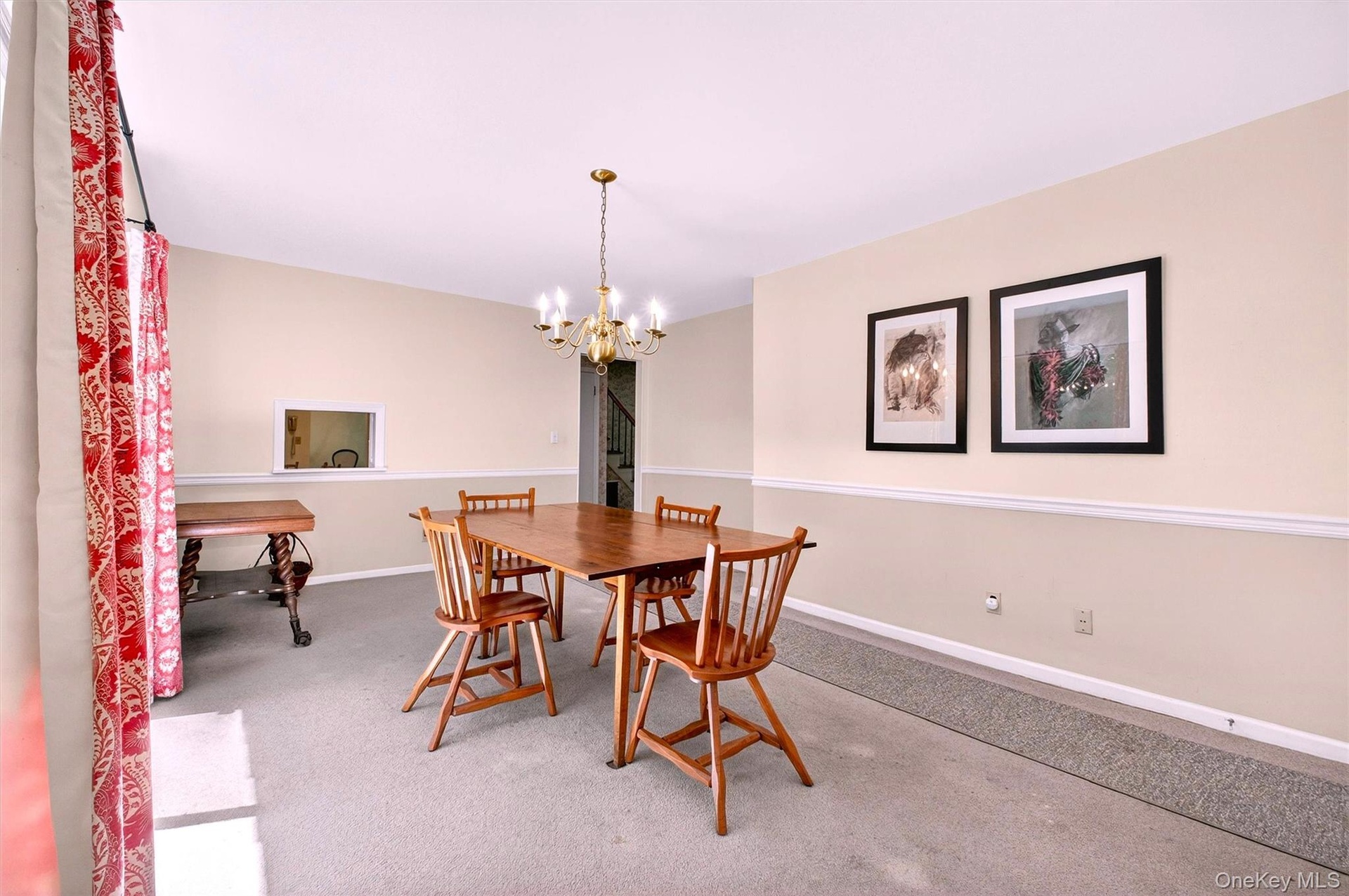 Formal dining room featuring a brass chandelier, two-tone painted walls with chair rail molding, and a pass-through window