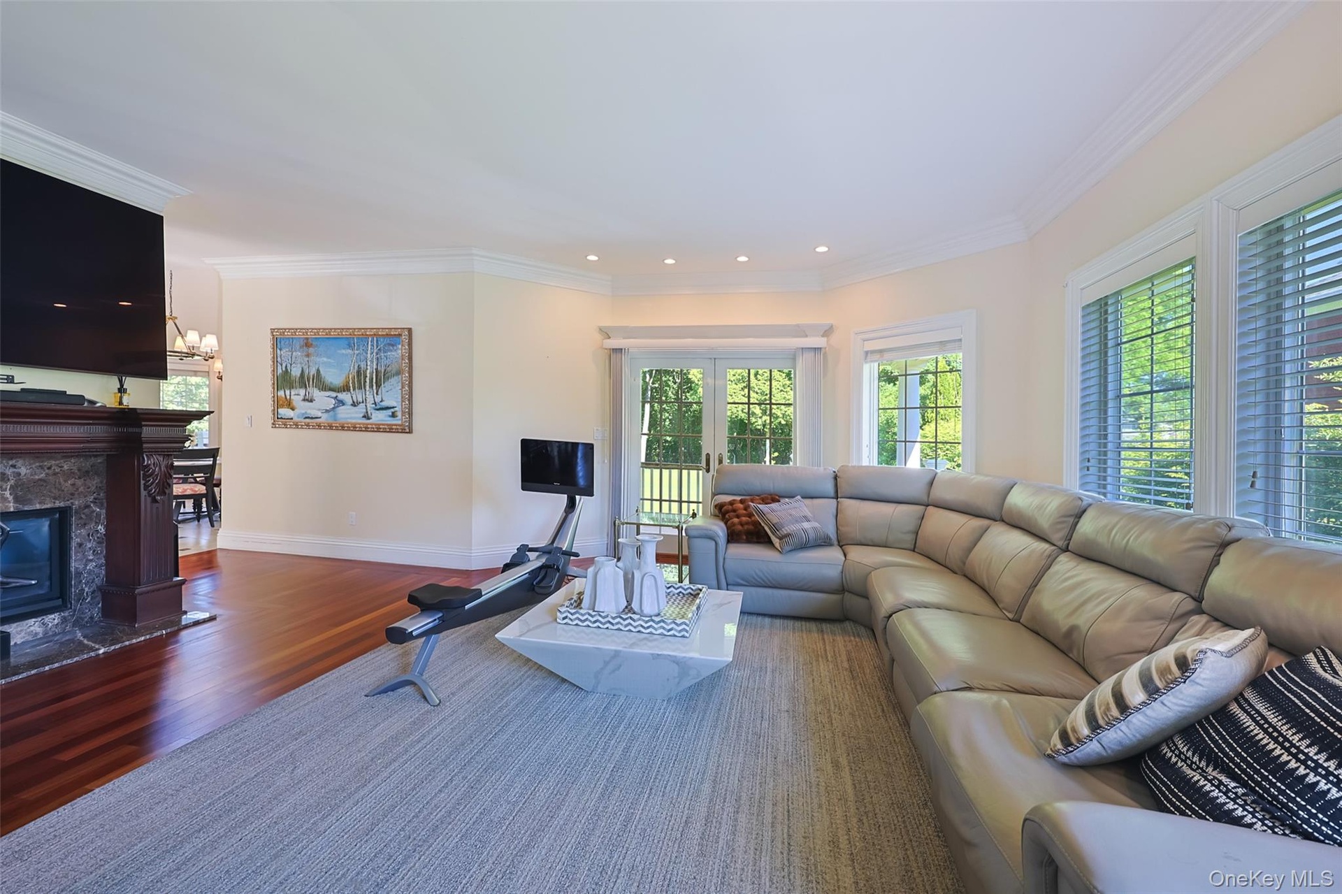 Living area featuring rich wood-finish flooring, a stone-surround fireplace with a dark wood mantel, recessed lighting, and crown molding