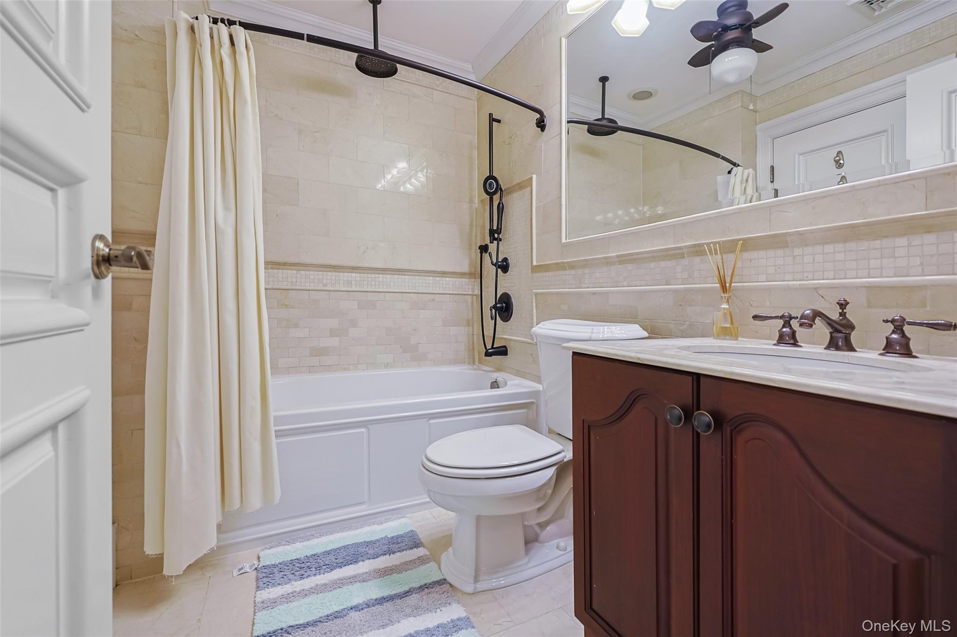 Bathroom featuring a dark wood vanity with a white countertop, a mirror with integrated lighting, a shower-tub combination with a dark-finish shower s