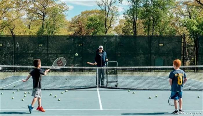 Full-size tennis court featuring a light blue playing surface, white demarcation lines, and a dark net