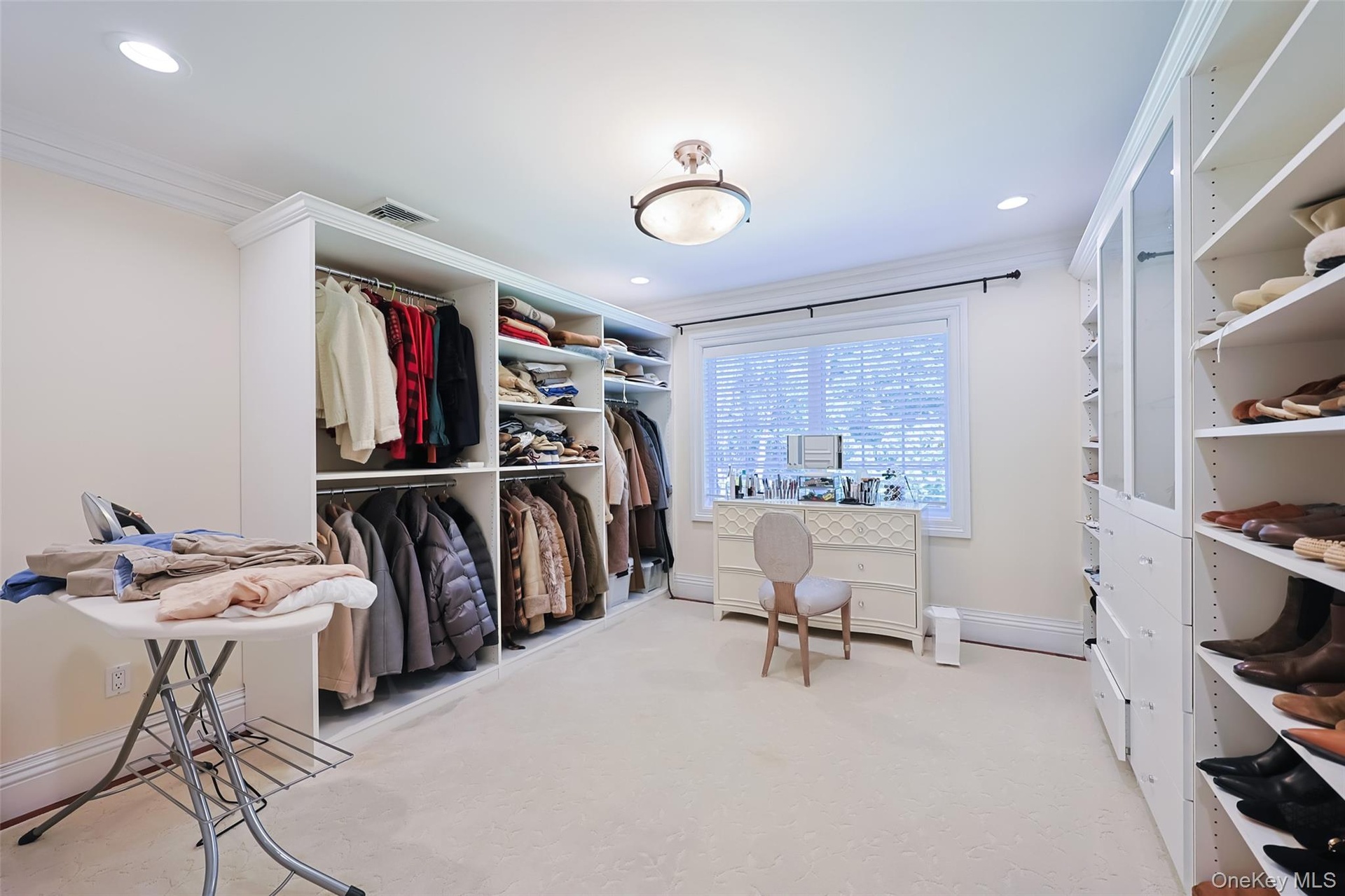 Spacious dressing room featuring extensive custom built-in cabinetry, recessed lighting, and a large window with blinds