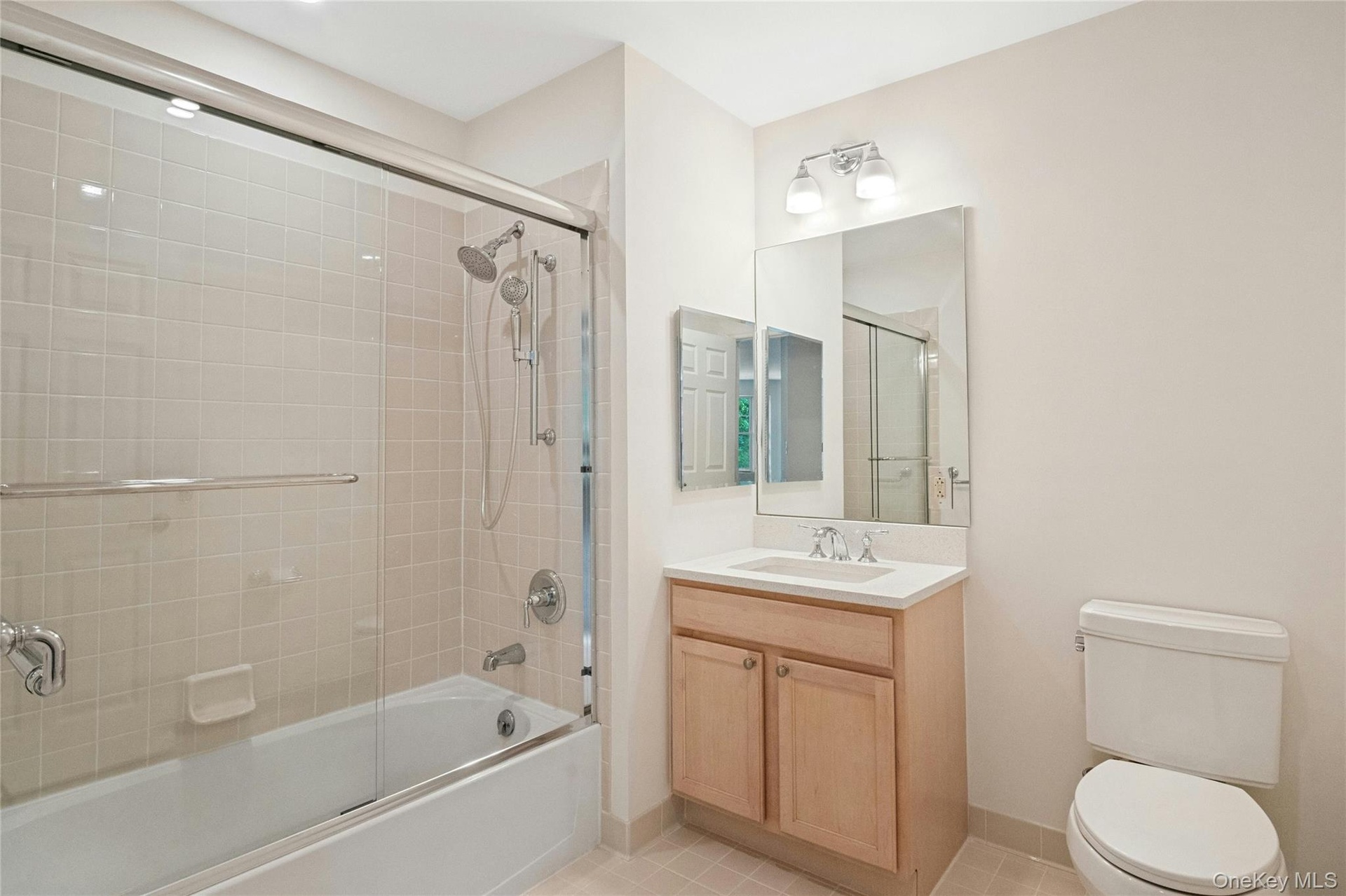 Updated bathroom with new glass shower doors, new bath light fixtures, vanity with wood cabinetry, and new white  quartz countertop