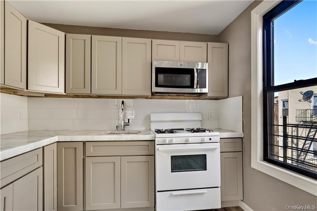 Top Floor Apartment Kitchen featuring taupe shaker-style cabinetry, white subway tile backsplash, light-toned countertops, and a stainless steel micro