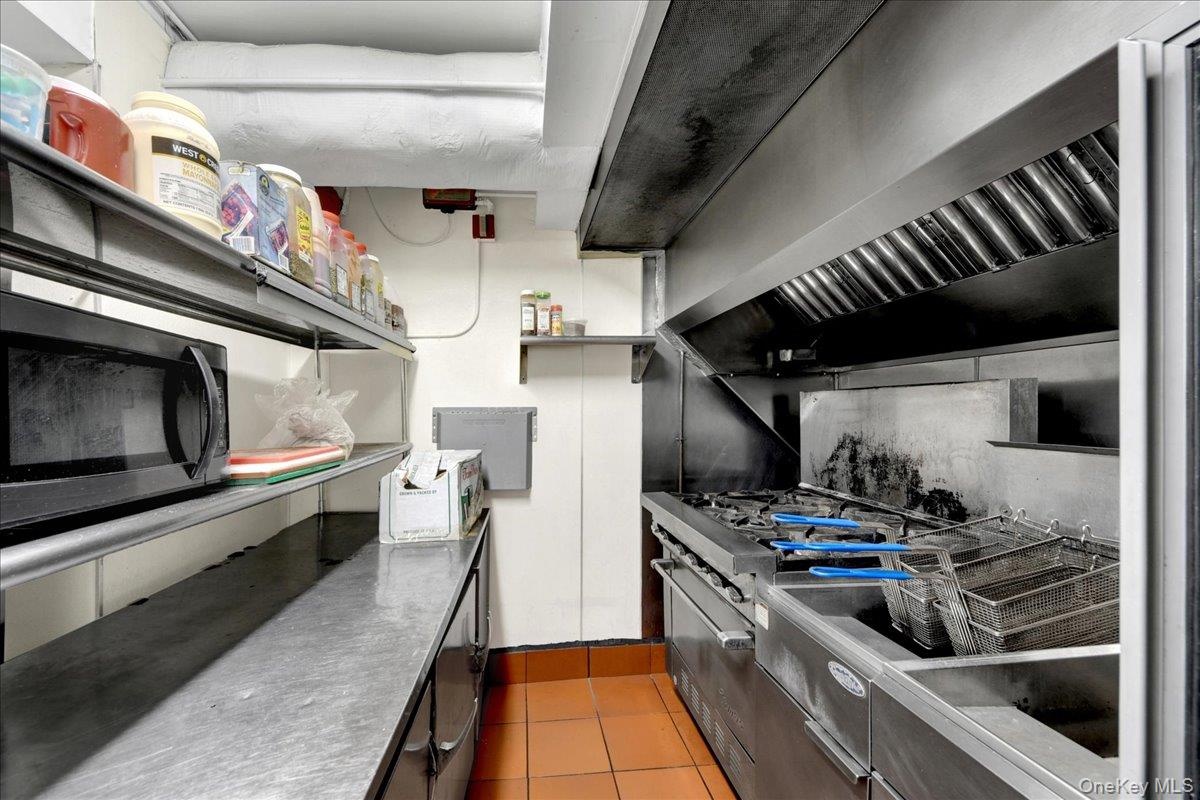 Commercial-grade stainless steel range with integrated fryer station, stainless steel exhaust hood, and industrial shelving