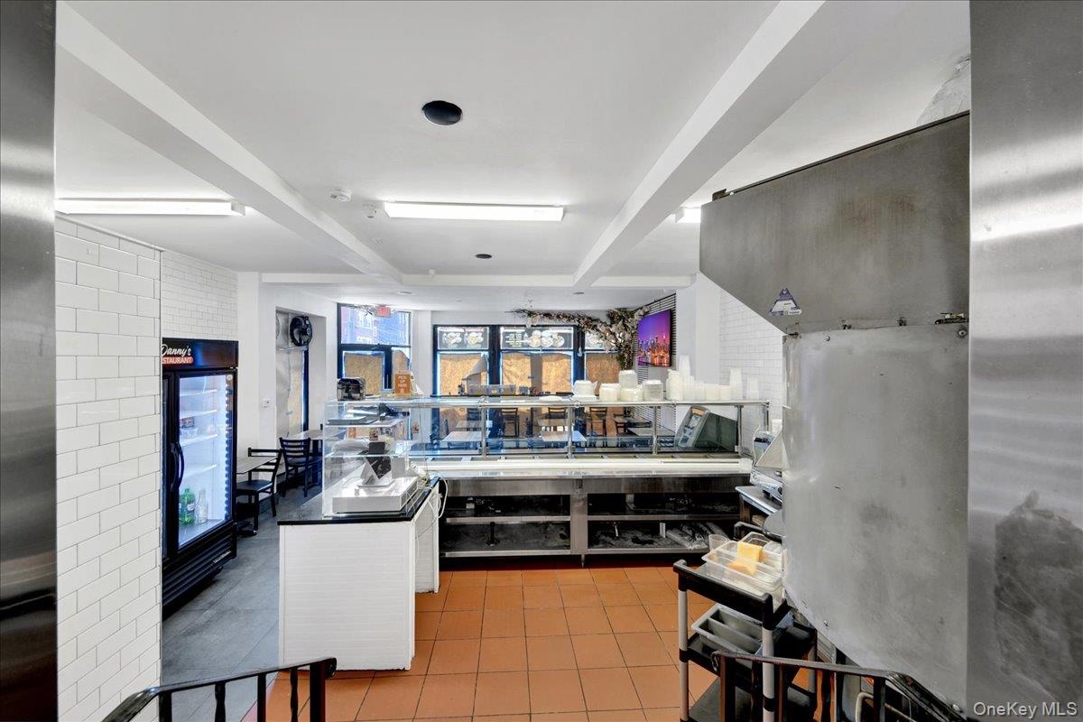 Commercial kitchen and service area featuring a stainless steel display counter, white subway tile wall, recessed lighting, and terracotta-toned floor