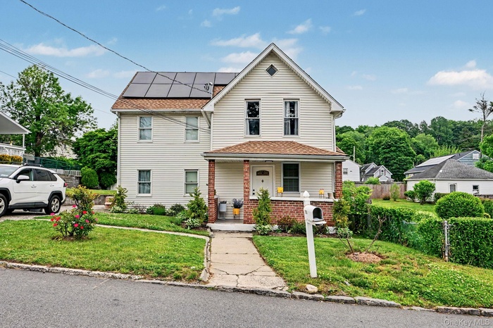Traditional two-story residence featuring light-colored siding, a covered front porch with brick pillars, and solar panels installed on the roof