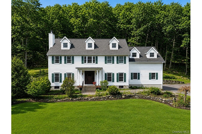 Classic white Colonial with green shutters set on a peaceful, wooded lot, offering timeless curb appeal and serene surroundings.