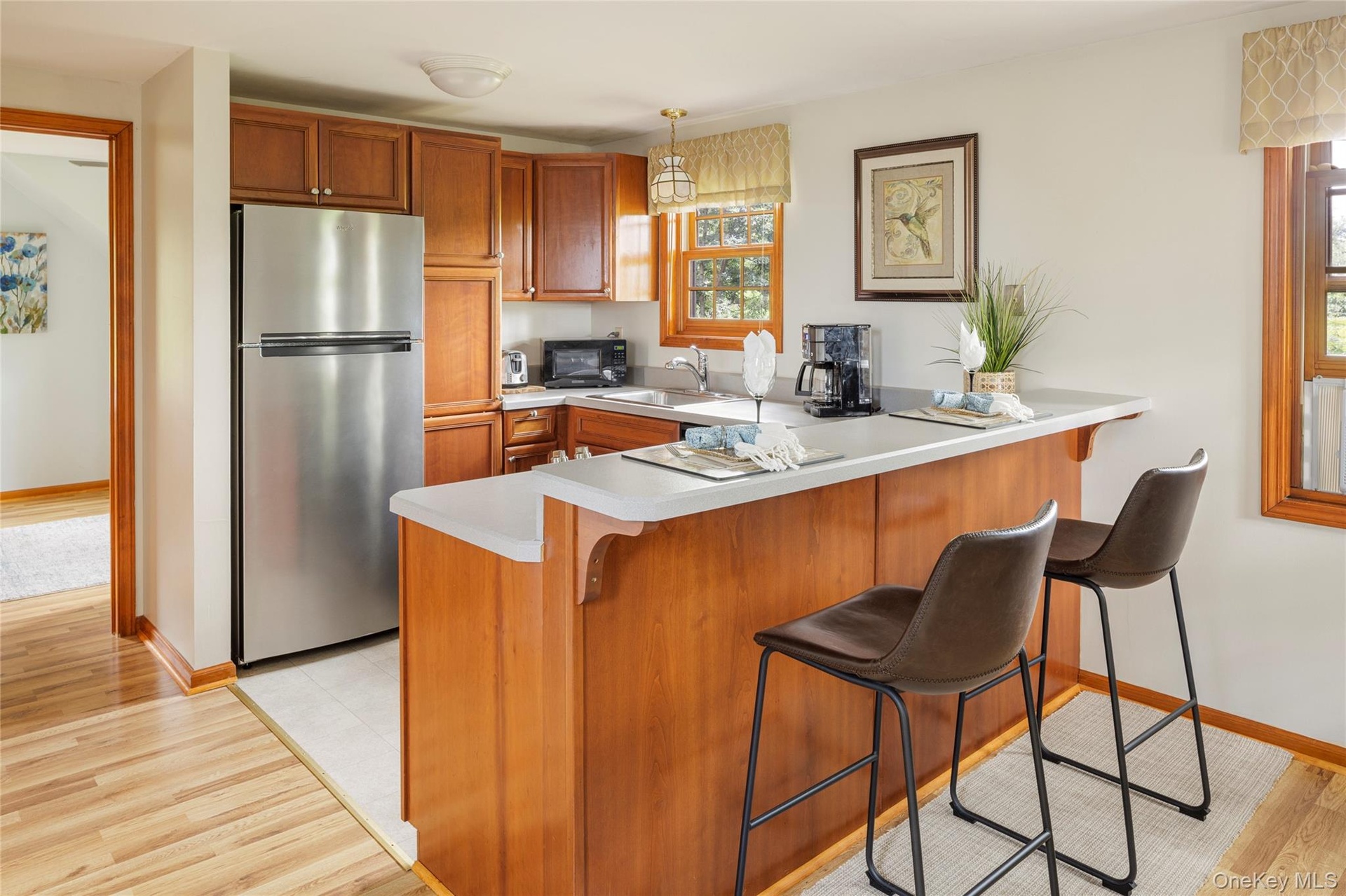 Kitchen featuring freestanding refrigerator, a peninsula, brown cabinetry, light countertops, and black microwave
