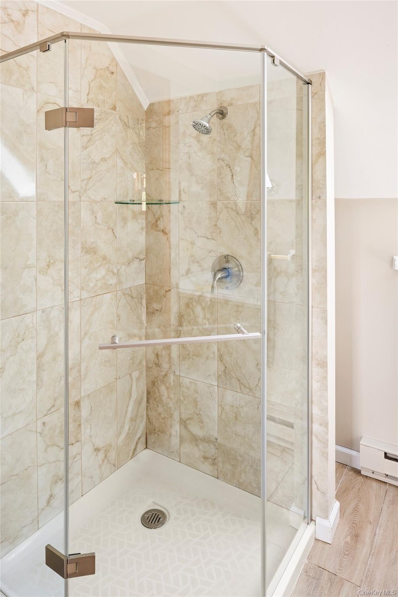 Bathroom with a shower stall, wood finished floors, crown molding, lofted ceiling, and a baseboard radiator