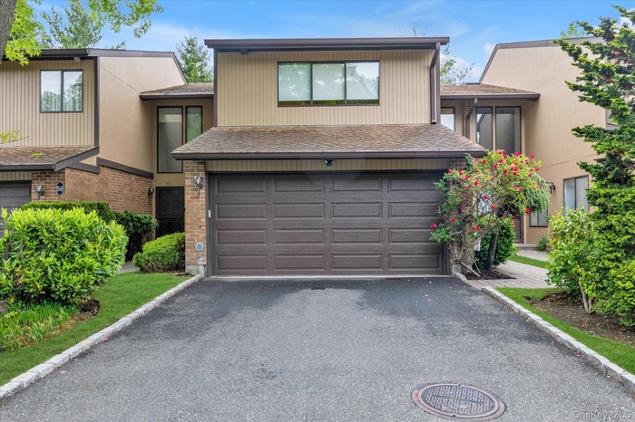 Two-story townhouse with a brown paneled garage door, asphalt driveway, and mature landscaping
