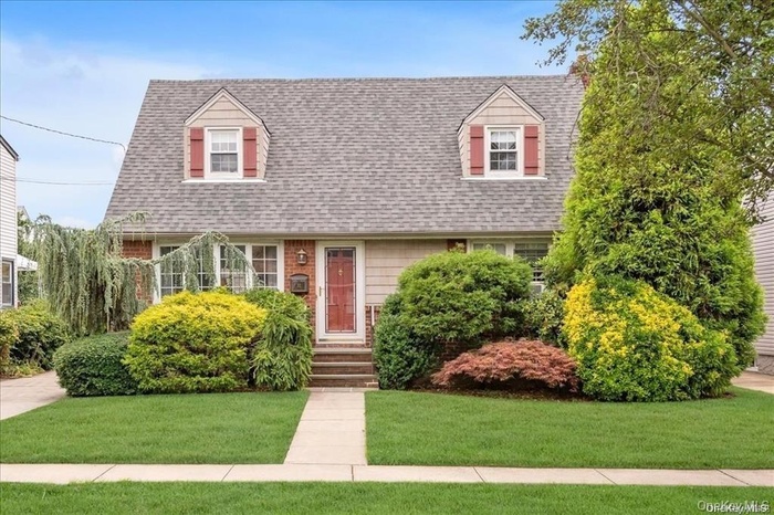 Front exterior featuring a gray shingle roof, two dormer windows with red shutters, and brick details