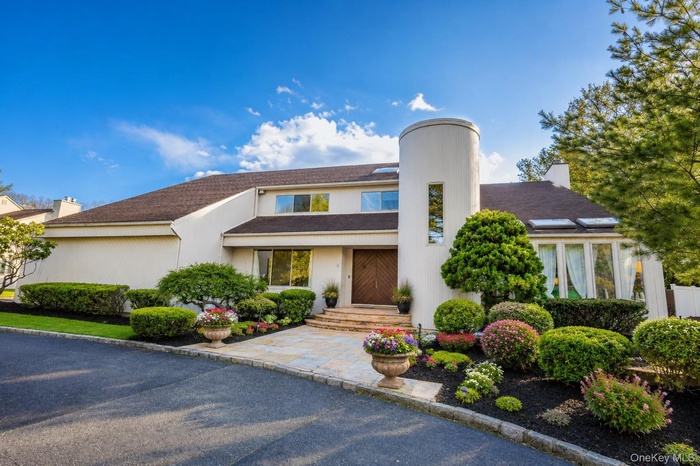 Contemporary stucco exterior featuring a prominent cylindrical tower with vertical window, double wooden entry doors, and a stone-paved walkway
