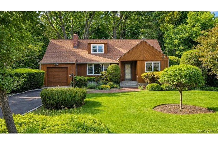 listing photo showing the front exterior, landscaped lawn, mature trees, and attached garage at 9 Sheep Pasture Lane in Huntington, NY 11743