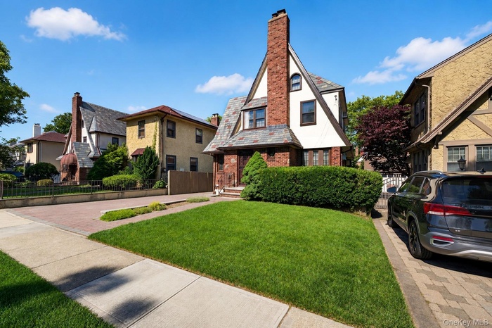 Tudor-style residence featuring a prominent brick chimney, multi-toned slate roof, and white siding with dark trim accents