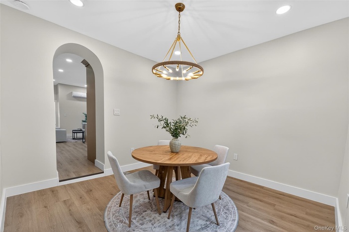 Dining area featuring a contemporary brass chandelier, wood-finish flooring, recessed ceiling lights, an arched entryway, and white baseboards