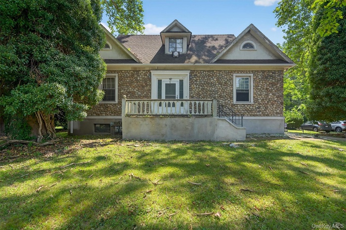 View of front of property with stone siding, a front lawn, and roof with shingles