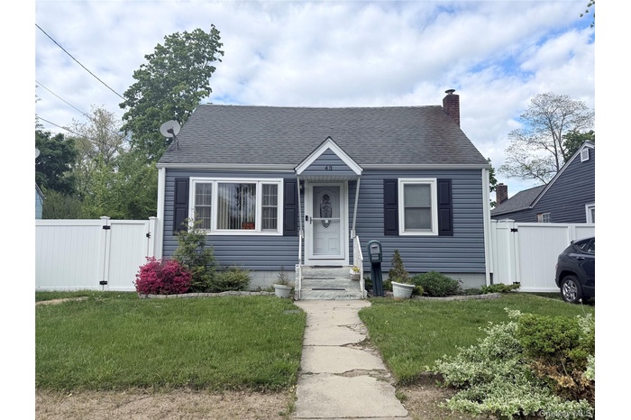 Charming residence featuring blue siding, a dark shingle roof, a brick chimney, and white privacy fencing