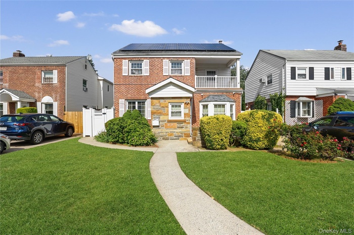 Brick and stone facade residence featuring solar panels, an upper-level balcony with white railing, and a bay window