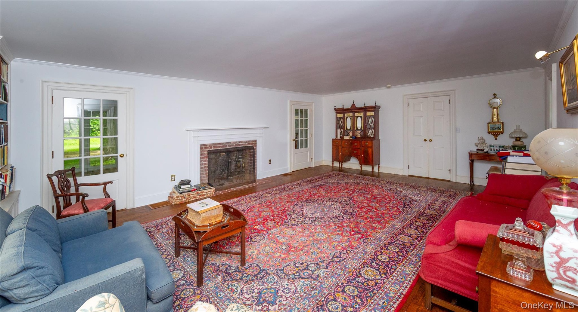 Spacious room featuring wood-finish flooring, a brick fireplace with a white mantel, and built-in shelving