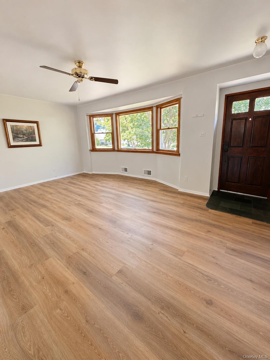Interior Family room featuring wood-finish flooring, a bay window with natural wood trim, and a ceiling fan