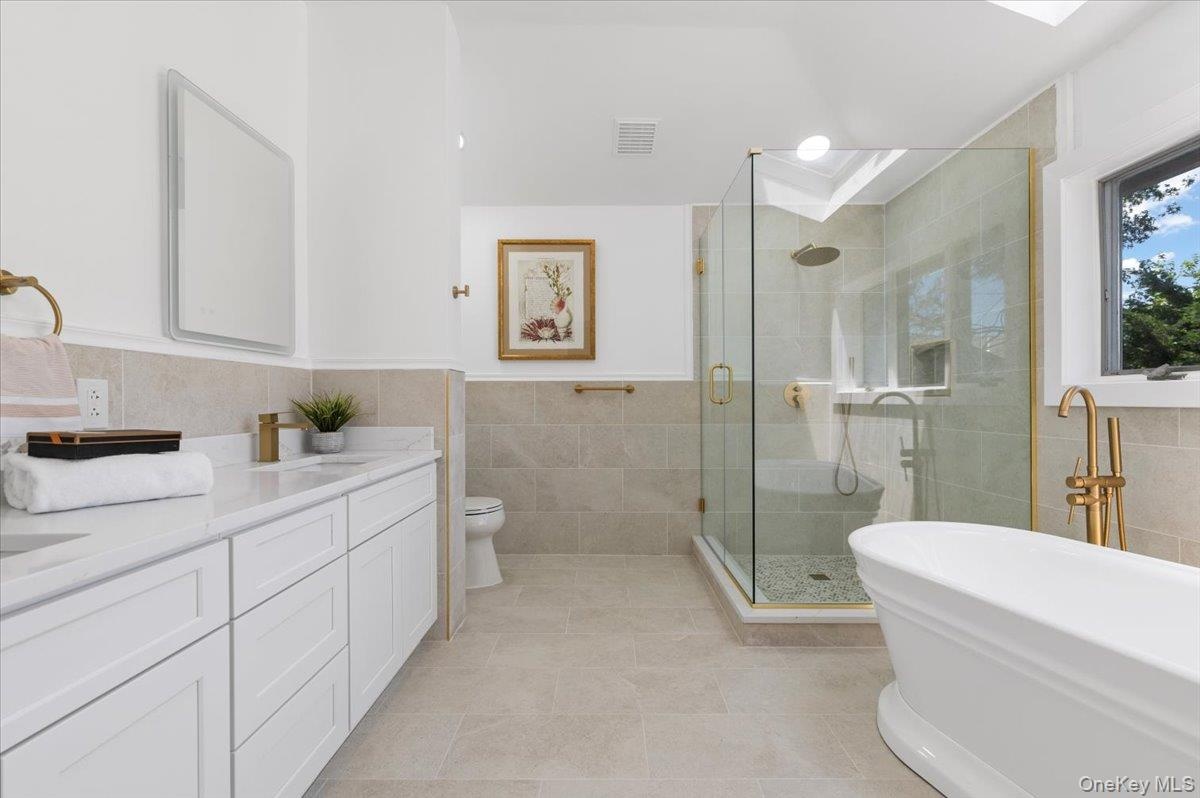 Full bathroom with tile walls, vanity, a stall shower, a freestanding bath, and tile patterned floors