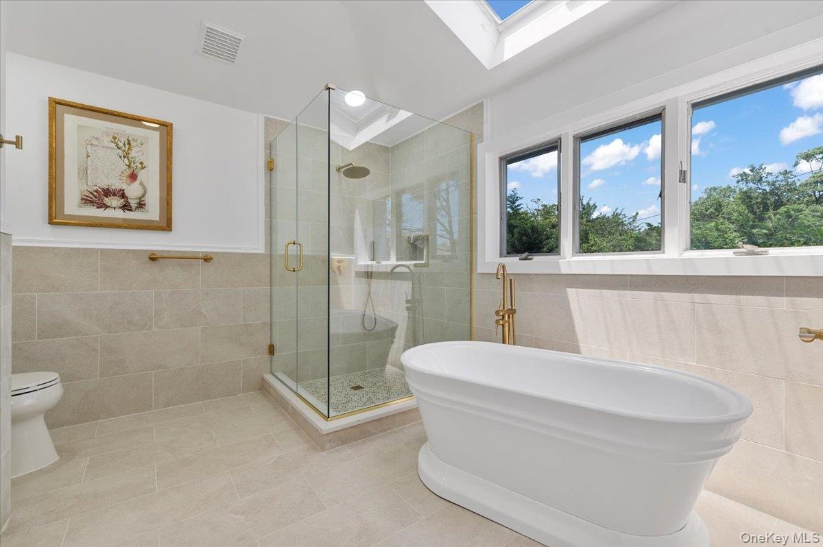 Bathroom with tile walls, a skylight, tile patterned flooring, a shower stall, and a freestanding tub