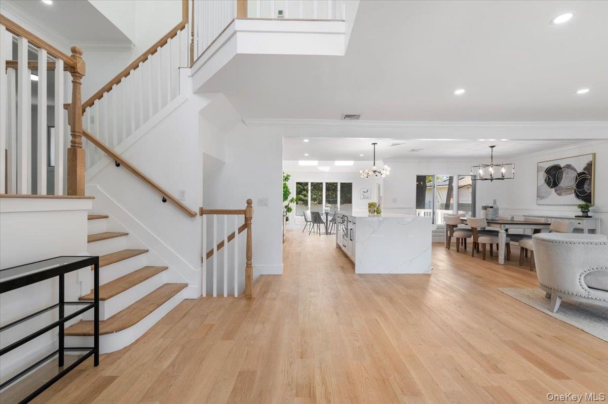 Living room with a chandelier, ornamental molding, light wood-type flooring, recessed lighting, and stairs