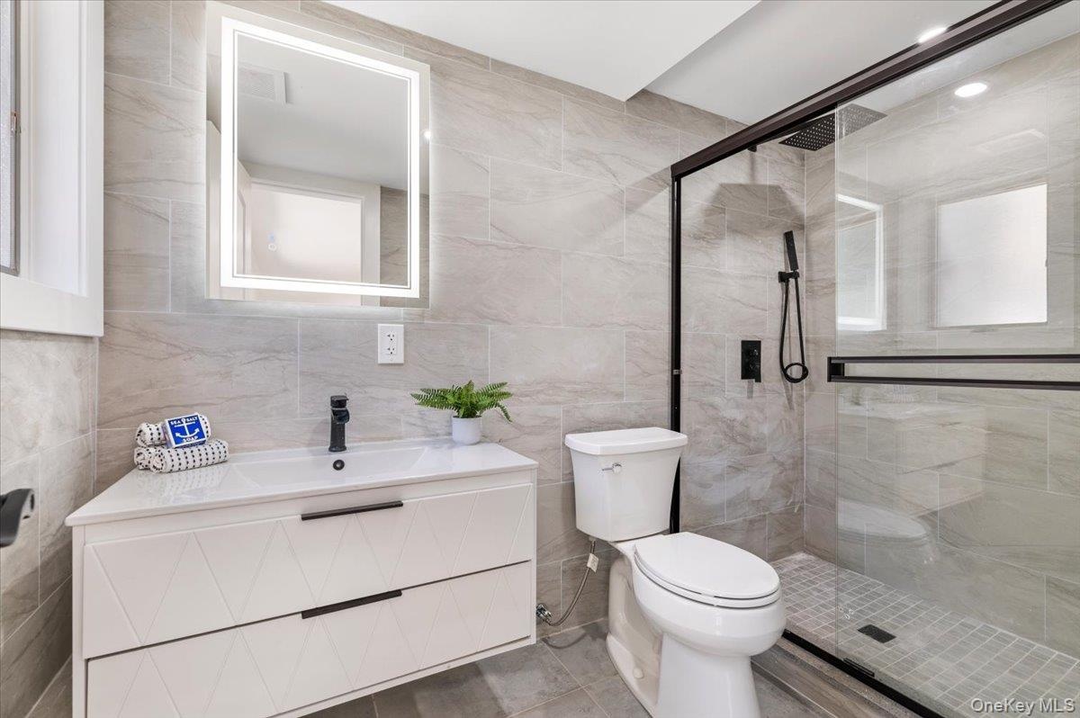 Bathroom with tile walls, vanity, a stall shower, and tile patterned flooring