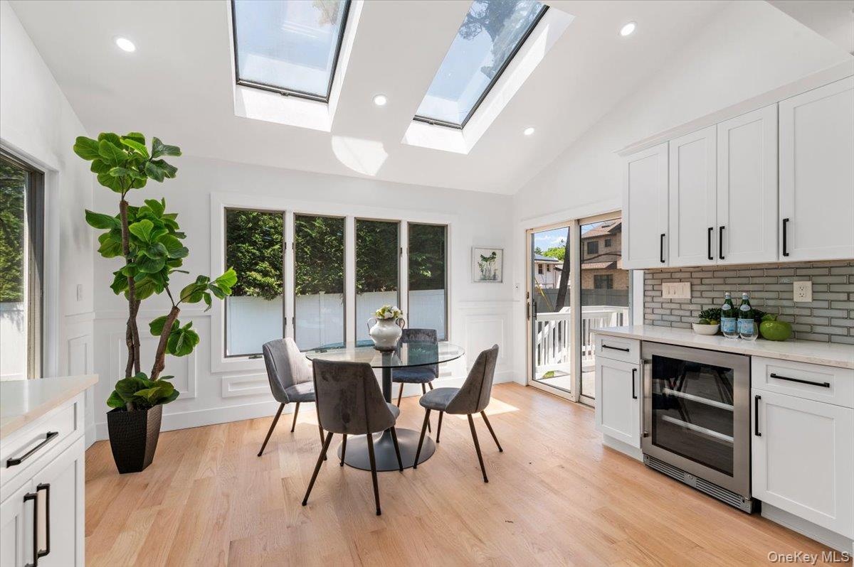 Dining space featuring wine cooler, a decorative wall, a skylight, light wood-style flooring, and a wainscoted wall