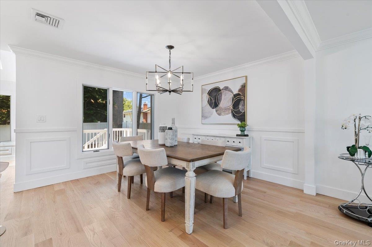 Dining room featuring a chandelier, a decorative wall, ornamental molding, light wood-style flooring, and wainscoting