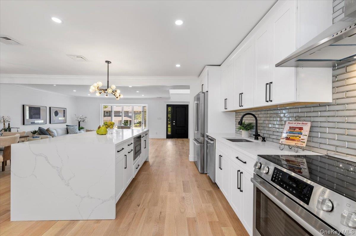 Kitchen featuring appliances with stainless steel finishes, wall chimney exhaust hood, light wood-type flooring, white cabinetry, and crown molding
