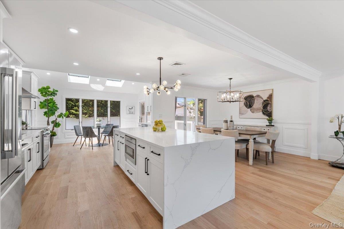 Kitchen featuring a chandelier, stainless steel appliances, white cabinetry, pendant lighting, and light wood finished floors