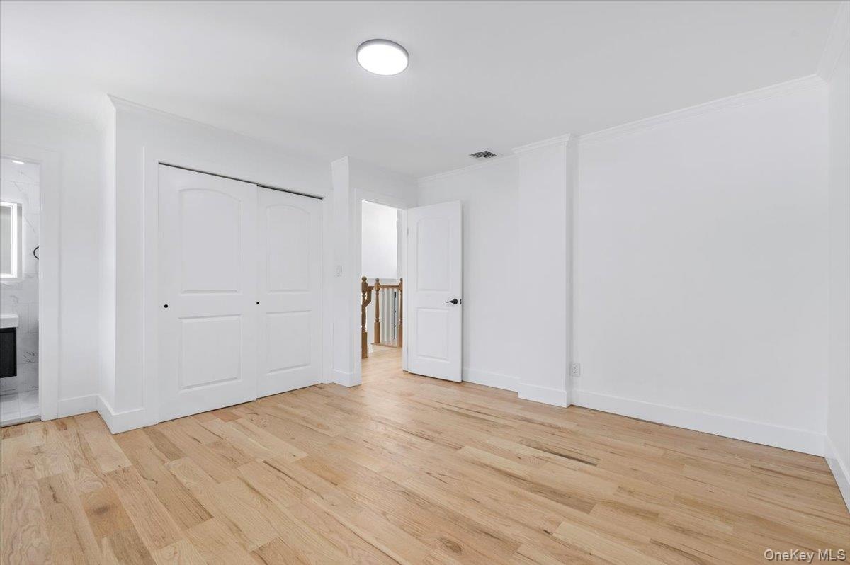 Unfurnished bedroom with light wood finished floors, crown molding, ensuite bathroom, and a closet